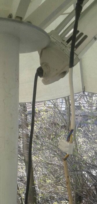 Infravärmare monterad på en parasollstolpe med kablar hängande, på en uteservering.