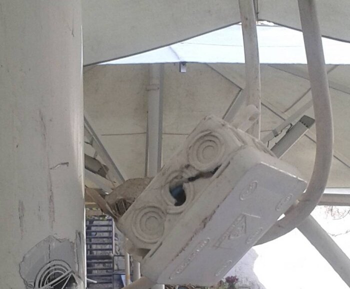 Vit installationsbox med kablar hängande på en parasollstolpe på en uteservering.