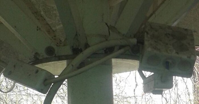 Elektrisk installation under parasoll på uteservering, visar fästa kablar och infravärmare anslutna till stolpe, förbättrad för att undvika lösa kablar.