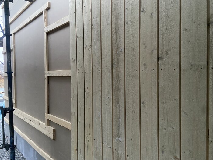 Trävägg under konstruktion med träpanel och skelett av reglar, del av pågående byggprojekt.