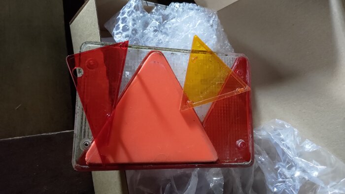 Baklykta för släpvagn med färgade glaspaneler i rött och orange, inklusive blinkers och dimljus, delvis förpackad i kartong med bubbelplast.