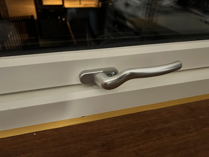 Fönsterhandtag monterat på en vit fönsterkarm i ett rum, dokumenterat för att byta till ett barnsäkert lås.