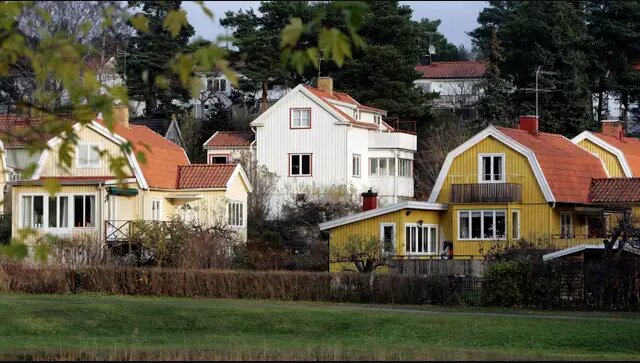 Hus med röd takpannor framför träd och buskar, varav ett hus har en altan på långsidan, fotograferat under en mulen dag.