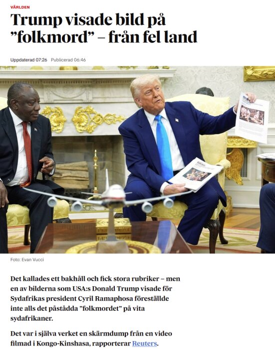 President i en kostym visar pappersbilder för en annan man i en mötesrumsmiljö med en guldfärgad dekoration i bakgrunden.