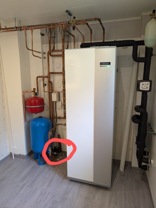Inkommande vatteninstallation i central badrumsdel med tryckströmbrytare omgiven av rör och en hydrofortank, markerad med röd cirkel.