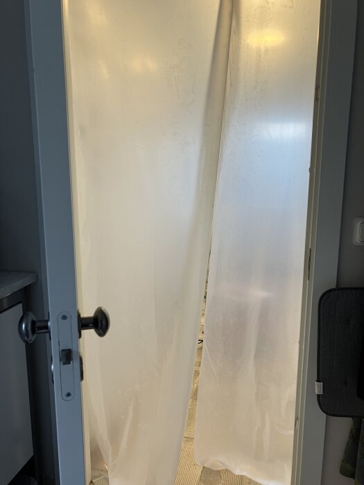 Plastfolie hänger i en dörröppning för att fånga damm under renovering.