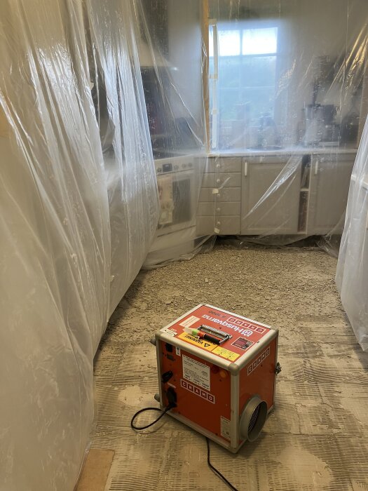 Renoveringsprojekt med plastskyddade ytor och dammfälla i ett rum under golvrenovering.