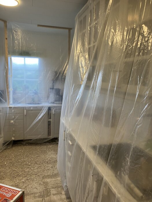 Kök insvept i plast för renovering, med dammfälla på plats och delvis bilat golv synligt.