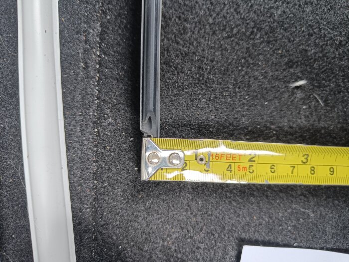Stängning av fönstertätningslist bredvid måttband som visar längd i centimeter, svart bakgrund.