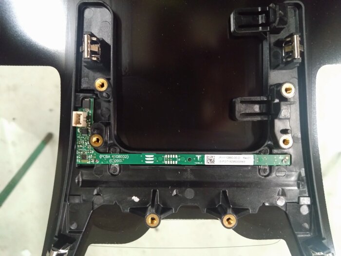 Regnsensor från en Tesla 3 med skruvfästen, elektroniskt kretskort, och monteringsdetaljer, fotograferad under byte av vindruta.