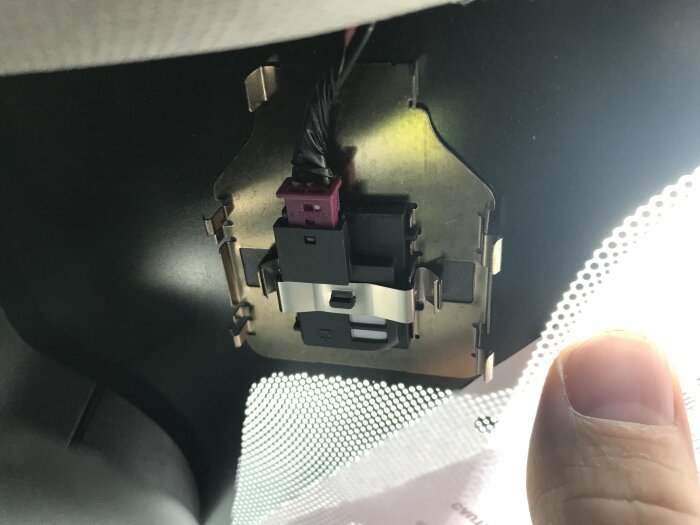 Fuktighetssensor monterad innanför bilens framruta med elektriska anslutningar synliga. Ett finger pekar mot sensorn.