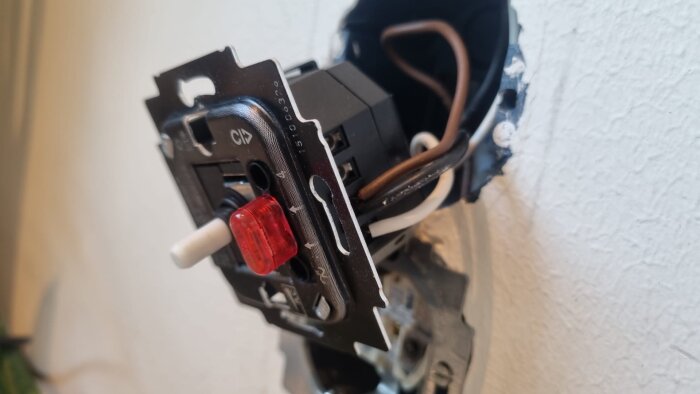 Närbild av en borttagen dimmeranslutning i en vägg, med synliga kablar och en röd komponent.