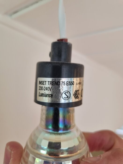 Spotlight med texten "INSET TREND 75 ES50 230-240V Lumiance" synlig på sockeln, hålls upp mot ett vitt tak.