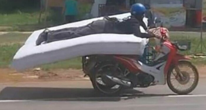 Person ligger på en madrass ovanpå en motorcykel medan den kör på en väg.