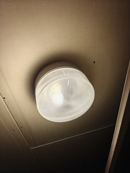 Rund takmonterad armatur med E27 sockel i garage, belyst inifrån med svag LED-lampa.
