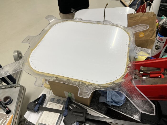 Flikigt fönsterglas förberett för montering i husvagn med glasfiber runt kanterna, klossar och verktyg i bakgrunden.