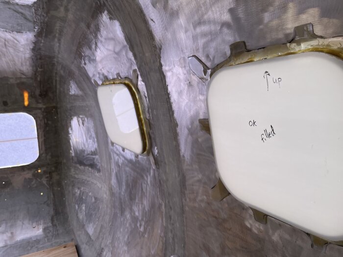 Fönster monterade inifrån husvagn med glasfiber och lim, två fönster synliga, en med text "up" och "ok filled", plast skydd borttagen.