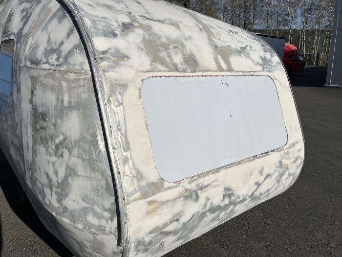En husvagn med nya fönster inpassade i plåten. Plåten är slipad och förberedd för montering. Husvagnen står utomhus.