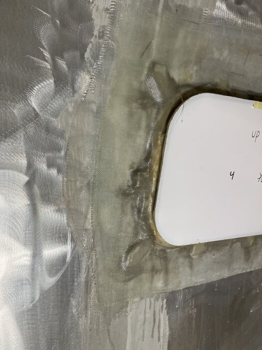 Fönster monterat med glasfiber och lim på husvagnsplåt, omgiven av plast och slipad yta, för fuktsäker och stabil infästning.