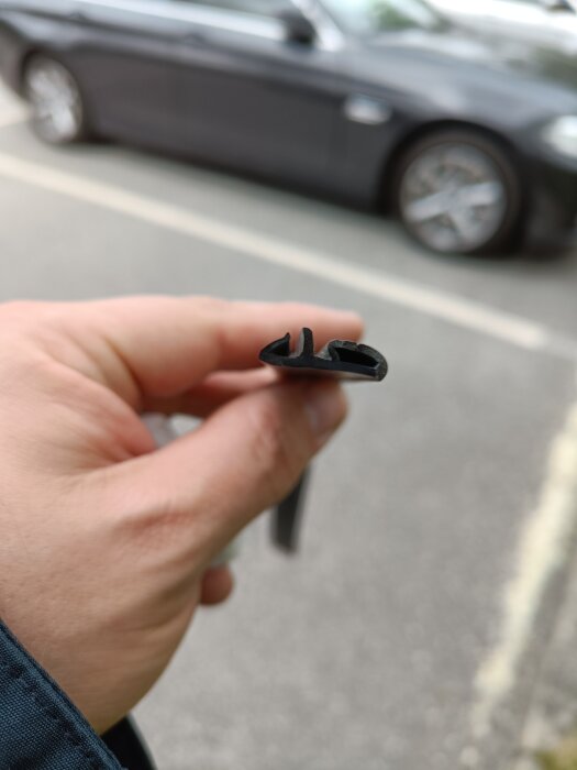 En hand håller en svart gummilist med ett bilhjul i bakgrunden.