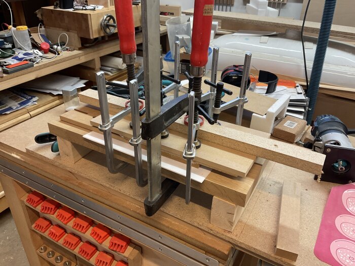 Träbearbetning i verkstad med flera tvingar som håller ihop träbitar under limning, verktyg och material i bakgrunden.