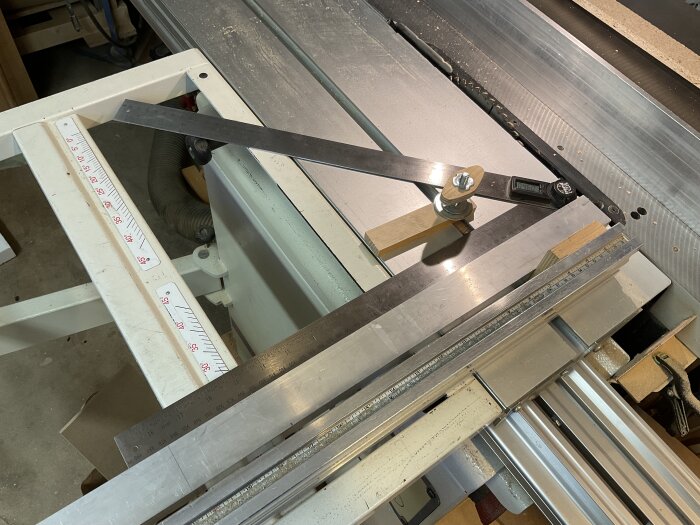 En digital vinkelmätare med 500 mm skänklar placerad på ett justersåg, tillsammans med en aluprofil och mätsticka i en träverkstad.