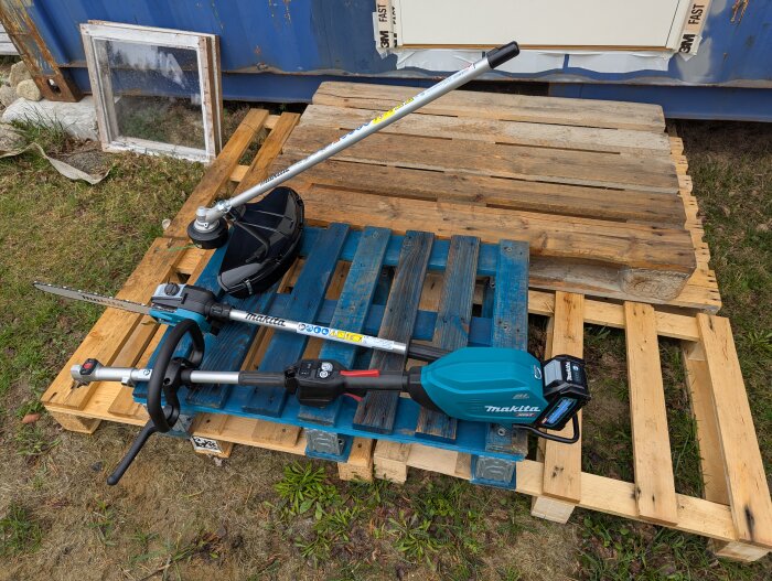 Makita multifunktionsenhet och grästrimmer på blå träpall utomhus, omgiven av gräs och trä.