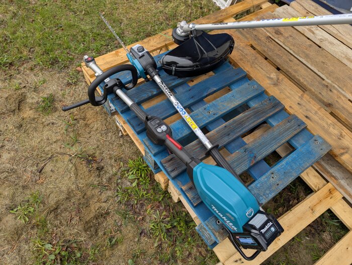 Multifunktionsenhet och grästrimmer på blå lastpall utomhus.