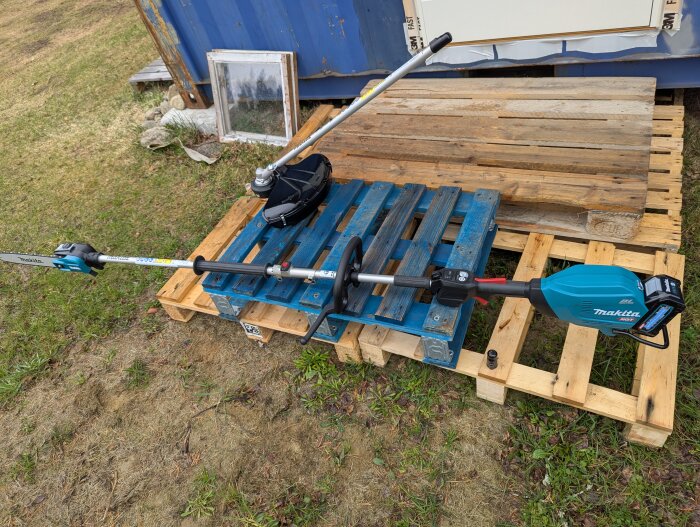 Multifunktionsenhet med grästrimmer och kedjesåg, placerad på en blå lastpall utomhus.