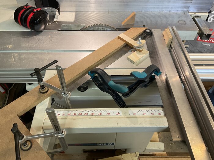 Arbetsstation med såg, träbitar sammanfogade med klämmor och lim för att skapa en jig för fräsning och kapning med exakta mått.