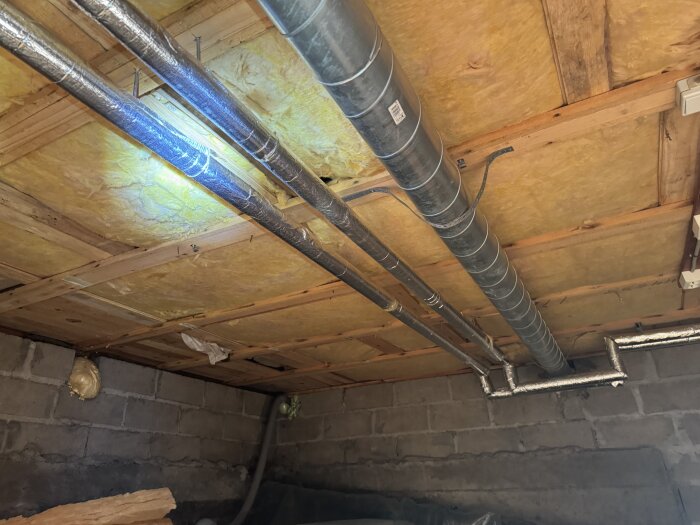 Tak med isolering och synliga metallrör i ett gammalt garage, pussel av träpaneler och betongväggar från tidigare renovering för 15 år sedan.