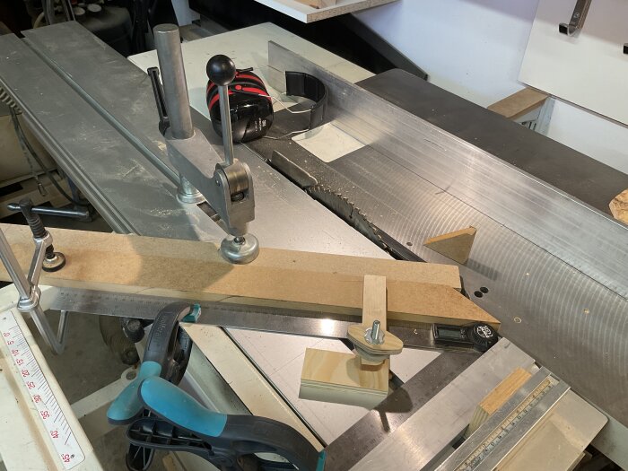 Arbetsbänk med spännanordning och aluprofil används för precisionskapning av trä; diverse verktyg och träbitar syns.