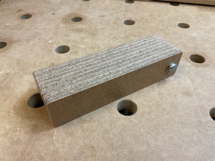 En packe fiberboard-remsor med en genomgående skruv på ett arbetsbord med hål. Används för att anpassa mellanlägg i en Moxon Vise.