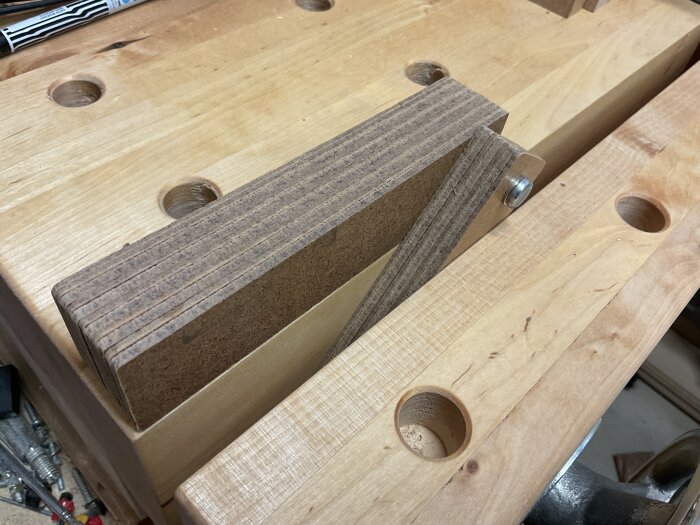 Packe fiberboard-remsor med genomgående skruv på träbord, används som justerbart mellanlägg för träarbete.