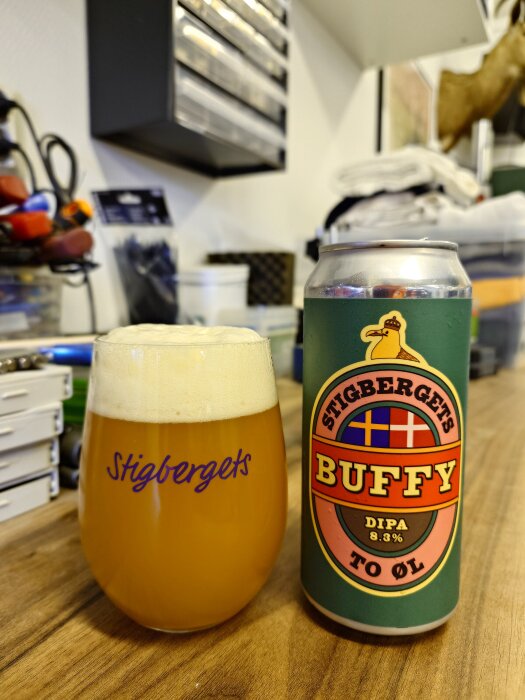 Ölglas med Stigbergets-logga och ölburk med Stigbergets Buffy DIPA 8.3% etikett på ett bord, verktyg i bakgrunden.
