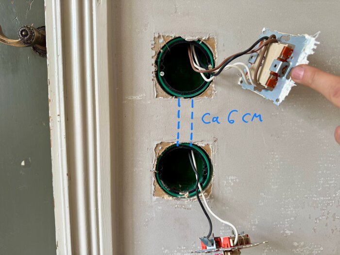 Två eldosor i en vägg med en hand pekande på en strömbrytare, markerad med text "ca 6 cm" mellan dosorna för ledningsdragning.