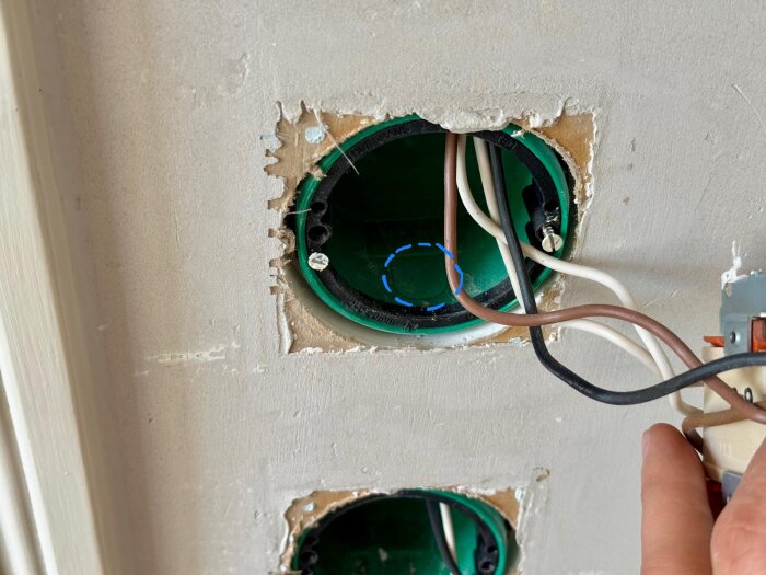Närbild på en väggdosa med elektriska kablar, en hand syns vid sidan, förbereder att dra nytt vp-rör.