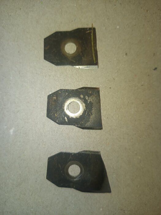 Trasiga gräsklipparknivar med slitage liggande på en grå yta.