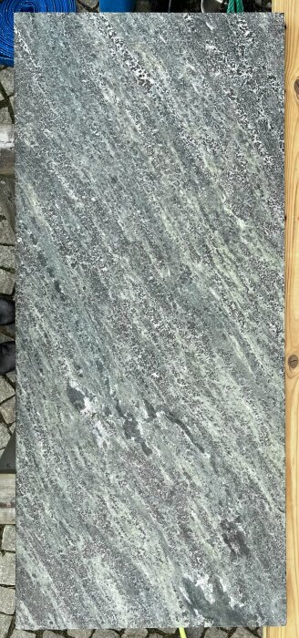 Skiva av kolmårdsmarmor med repor och patina, storlek 26x530x1200 mm, använd för golvgjutning vid vedspis.
