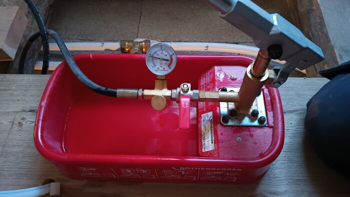 En röd provtryckningspump från Rothenberger, använd för att testa trycket i rörsystem, står fylld med vatten på en arbetsbänk.