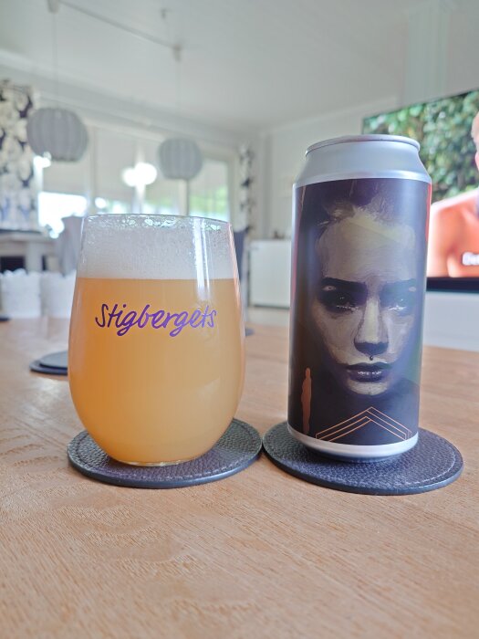 Ett glas öl med Stigbergets logga bredvid en burk med konstnärligt ansikte i ett ljust rum.