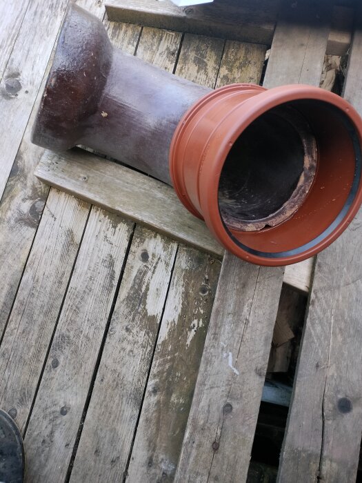 Gammalt keramikrör och nytt plaströr ovanpå träplankor, används vid avloppsreparation.