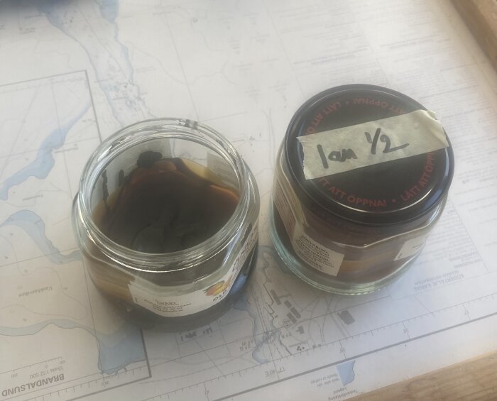 Två glasburkar med hemlagat trätjära och bivaxspackel, en öppen med synligt innehåll, står på en karta.