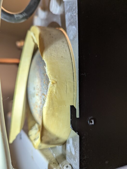 Närbild av ett gulnat värmepaket med något förändrad form och rost på ytan, monterat på en enhet.