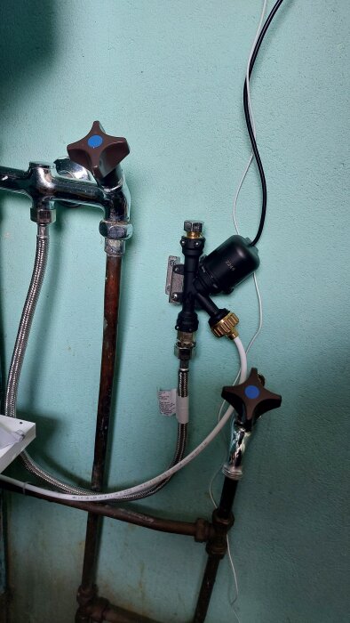 Vattenrör med ventiler, anslutningar och en installerad Knycklan-ventil från IKEA syns mot en ljusblå vägg.