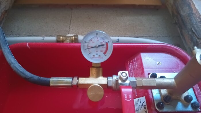 En tryckmätare som visar 5 bar på en röd kompressor eller pump med kopplingar och en slang.