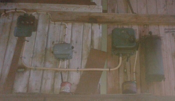 Bild av gamla elektriska komponenter och rör på en trävägg i ett nedlagt sågverk, del av historisk industriell infrastruktur.