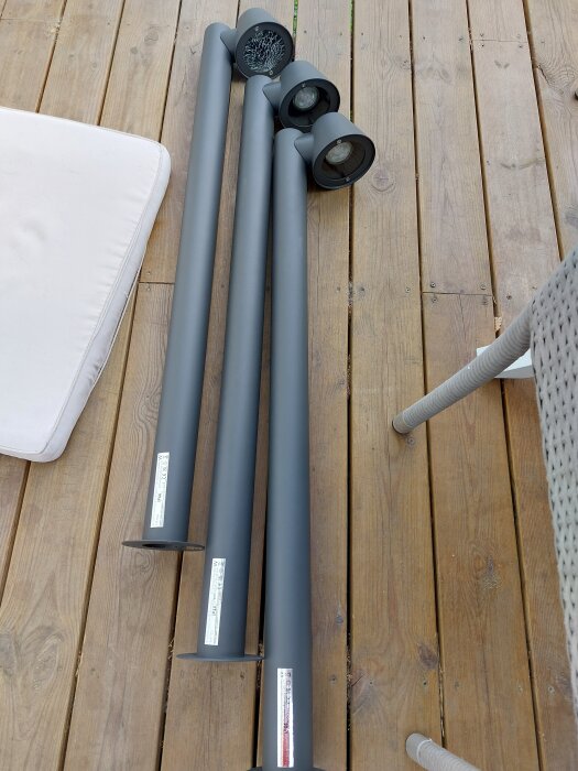 Tre gråa metallpollare ligger på en altan i trä, redo för användning i markstensprojekt.