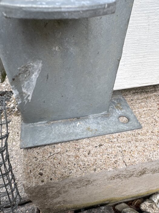 Stolpsko på betongmur med synlig skada och saknad understöd under ena sidan.