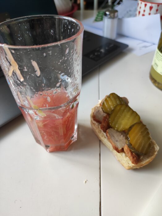 Glas med rabarbersoppa och en smörgÄs med köttbullar och inlagd gurka pÄ ett bord.
